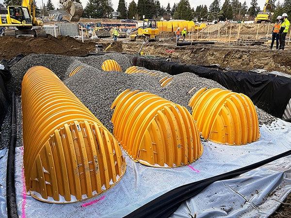 a large hole at a construction site has material under yellow curved pieces that are partially covered with gravel
