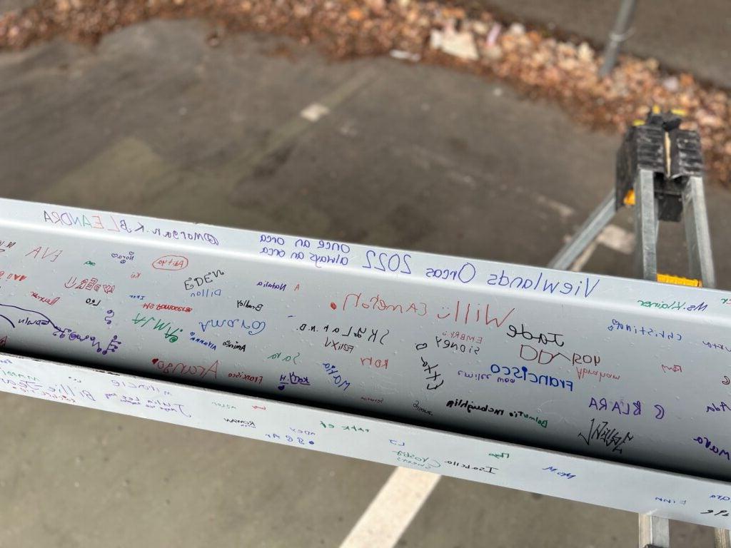 a white steel i-beam has signatures in various colors on it