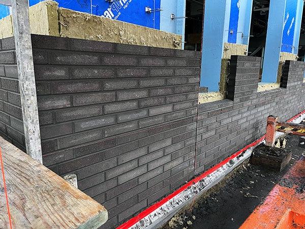 a masonry wall going onto a building with varying colors of bricks