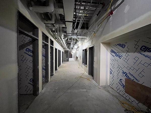 a hallway under construction with large openings on each side, ceiling structure showing, and wall board with tape and mud