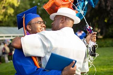 A student in cap and gown hugs an adult during a graduation ceremony 