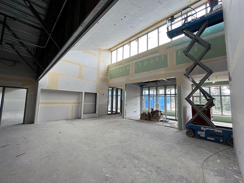 a large volume 2-story room is under construction with taped but not finished wall board, windows and doors, and the bottom part of a scissor lift visible