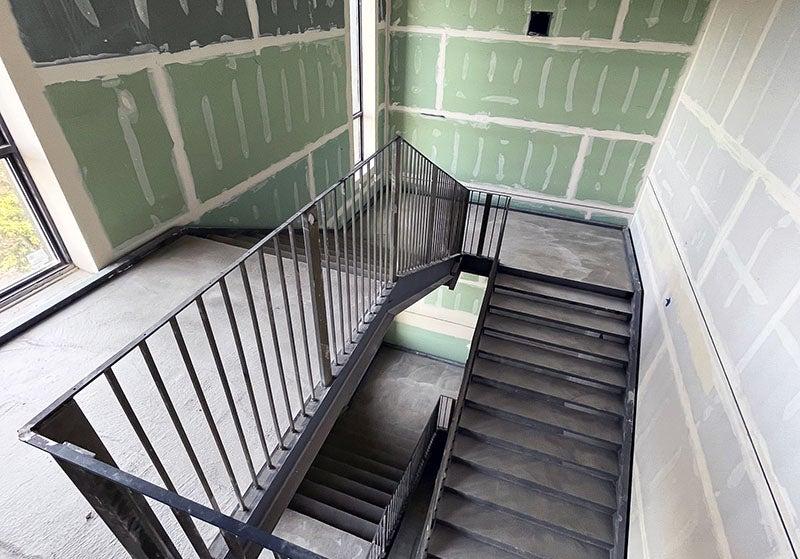 a concrete stairway with green wallboard that has tape and mud on it