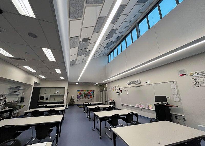 a large clasroom has tables and a white board with transom windows and ceiling lights